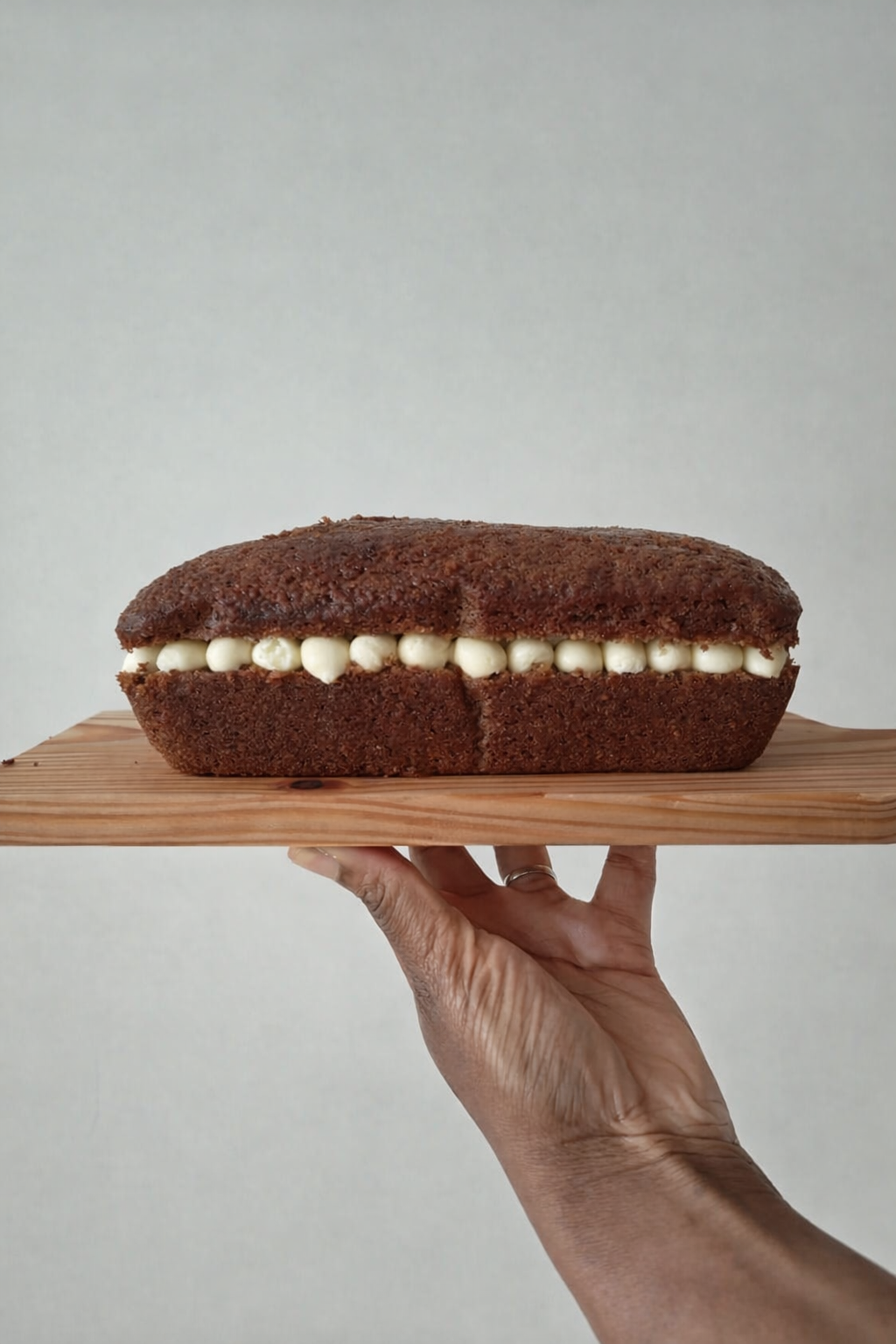 Carrot cake loaf with Philadelphia cream cheese buttercream frosting held on a wooden board by a hand against a neutral background