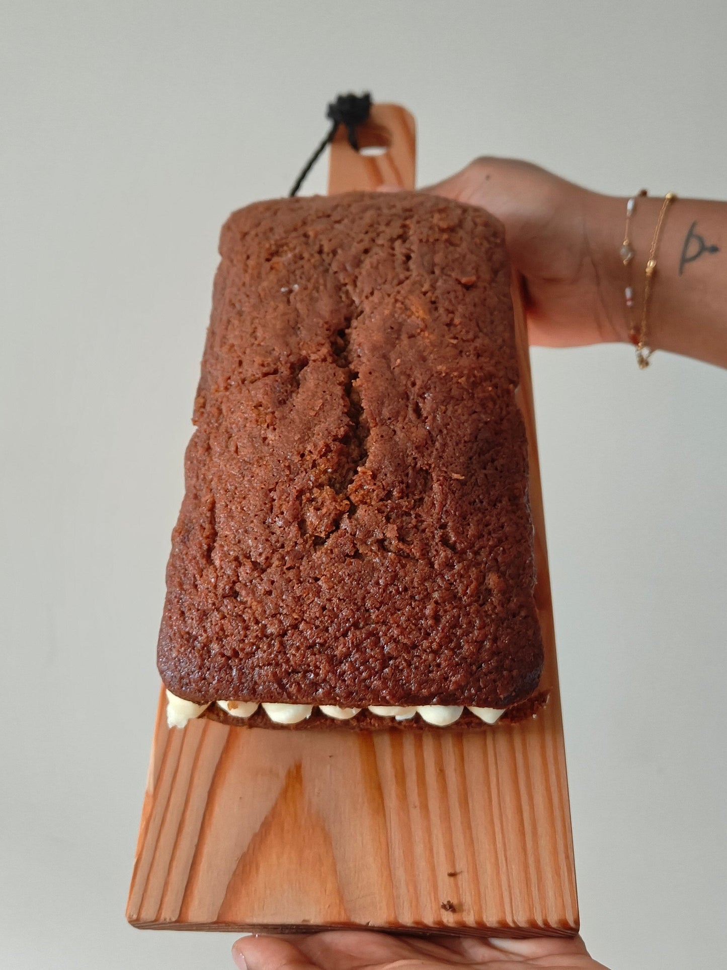 Carrot cake loaf with Philadelphia cream cheese buttercream frosting held on a wooden board by two hands against a neutral background