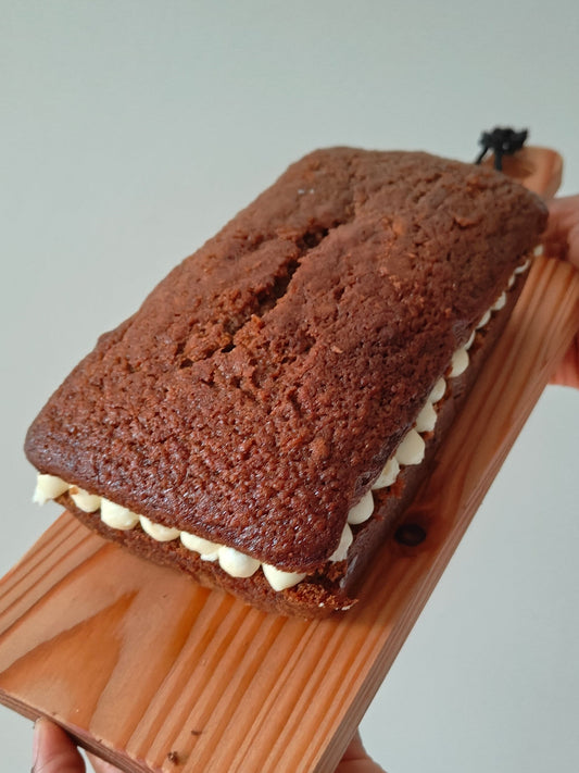 Carrot cake loaf with Philadelphia cream cheese buttercream frosting held on a wooden board by two hands against a neutral background