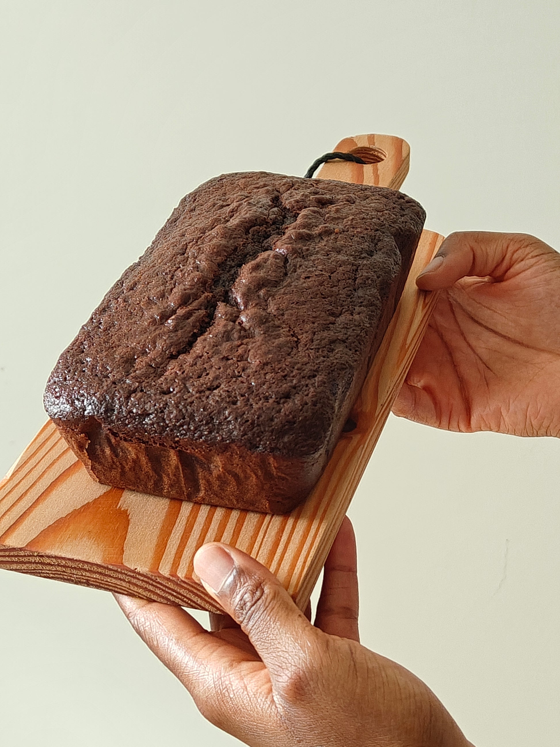 Chocolate loaf cake on a wooden board held by two hands against a light background