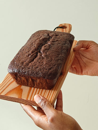 Chocolate loaf cake on a wooden board held by two hands against a light background