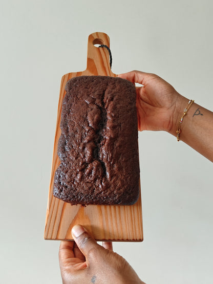 Chocolate loaf cake on a wooden board held by two hands against a light background