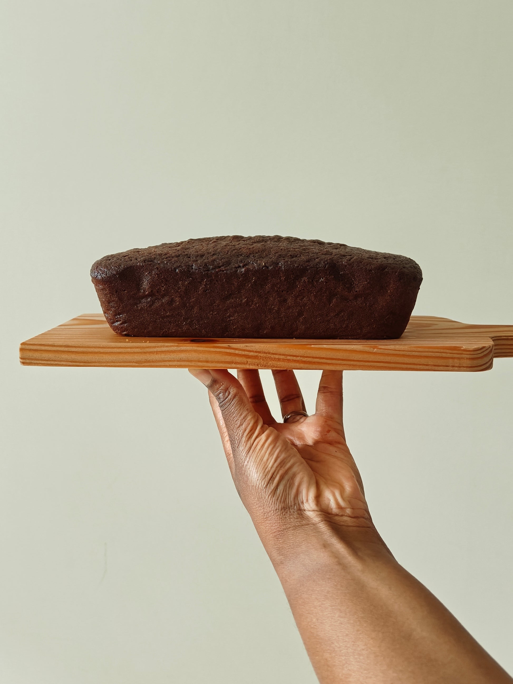 Chocolate loaf cake on a wooden board held by a hand against a light background