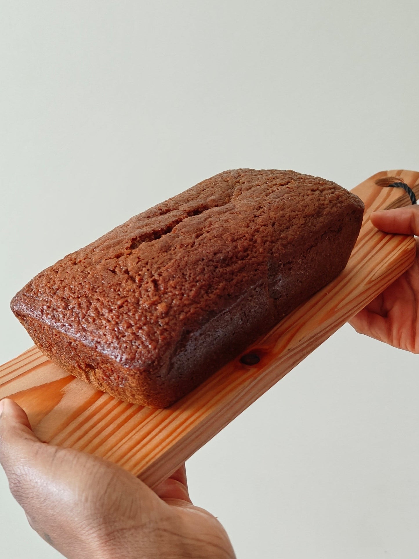 Carrot cake loaf held on a wooden board by two hands against a neutral background