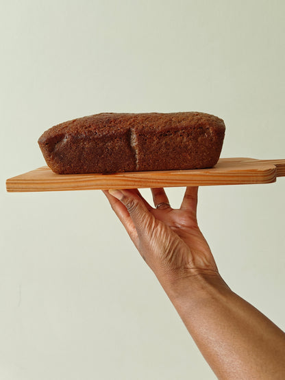 Carrot cake loaf held on a wooden board by a hand against a neutral background