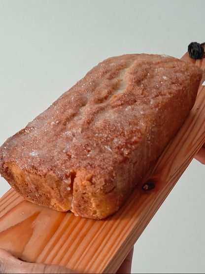 Drizzle loaf cake with lime and ginger on a wooden board held by two hands against a plain background