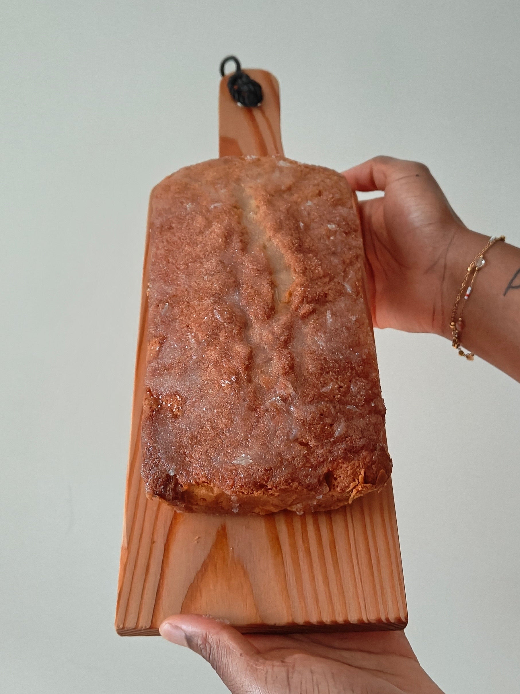 Drizzle loaf cake with lime and ginger on a wooden board held by two hands against a plain background