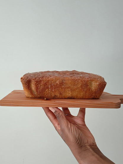 Drizzle loaf cake with lime and ginger on a wooden board held by a hand against a plain background