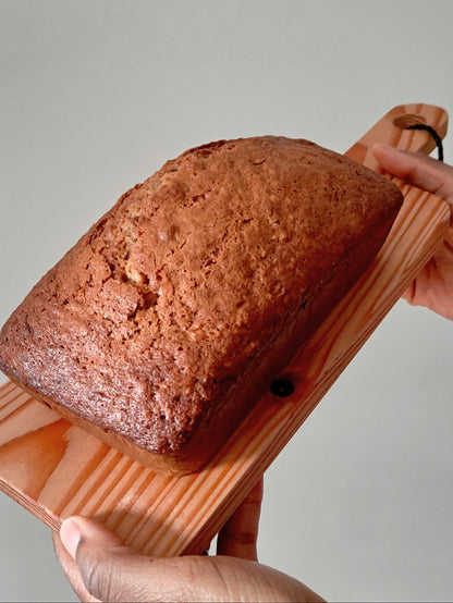 Loaf of banana bread on a wooden board held by two hands against a neutral background