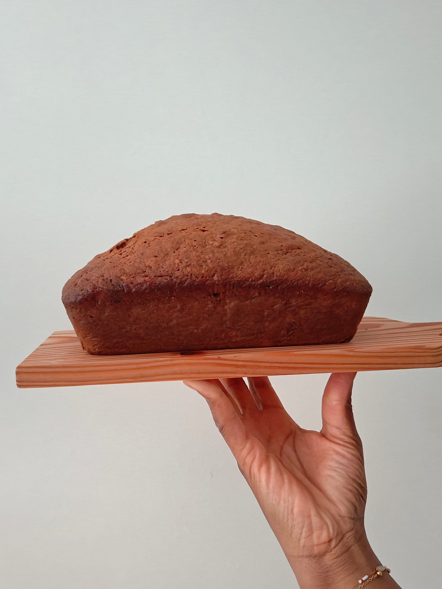 Loaf of banana bread on a wooden board held by a hand against a neutral background