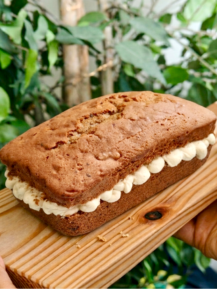 Coffee loaf cake with mascarpone buttercream filling on a wooden board held by two hands against a green foliage background