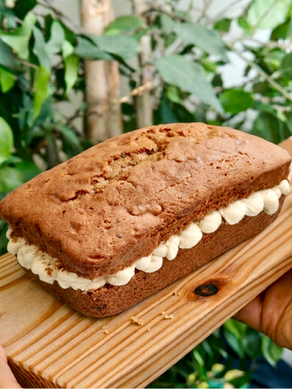Coffee loaf cake with mascarpone buttercream filling on a wooden board held by two hands against a green foliage background
