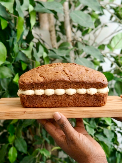Coffee loaf cake with mascarpone buttercream filling on a wooden board held by two hands against a green foliage background