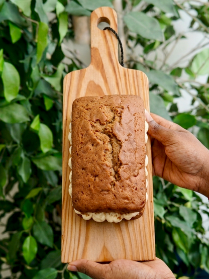 Coffee loaf cake with mascarpone buttercream filling on a wooden board held by two hands against a green foliage background