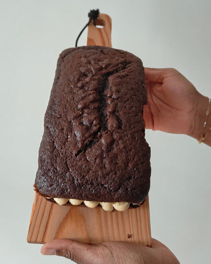 Chocolate loaf cake with mascarpone buttercream filling on a wooden board held by a hand against a white background
