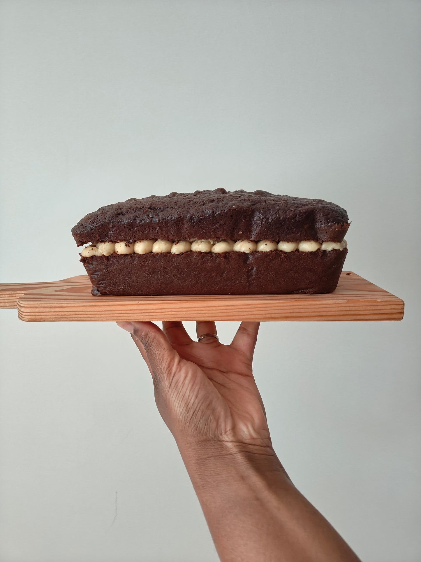 Chocolate loaf cake with mascarpone buttercream filling on a wooden board held by a hand against a white background